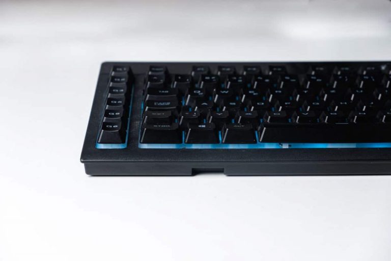 A low profile shot of a black mechanical keyboard with keys backlit with blue light
